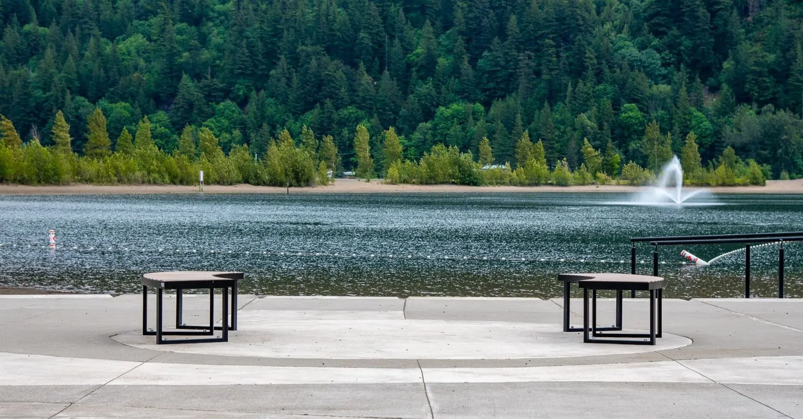 Two curved benches provide seating near the water's edge. The benches feature recycled plastic lumber tops and black powder-coated frames, offering a place to relax and enjoy the lakeside view.