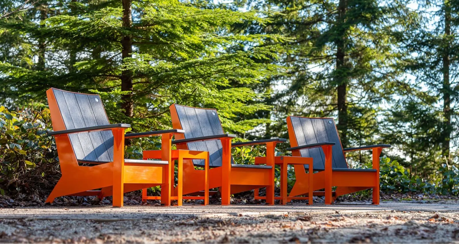 Three JEM Lounge Chairs provide comfortable seating in a park setting. The chairs feature recycled plastic lumber and powder-coated frames.