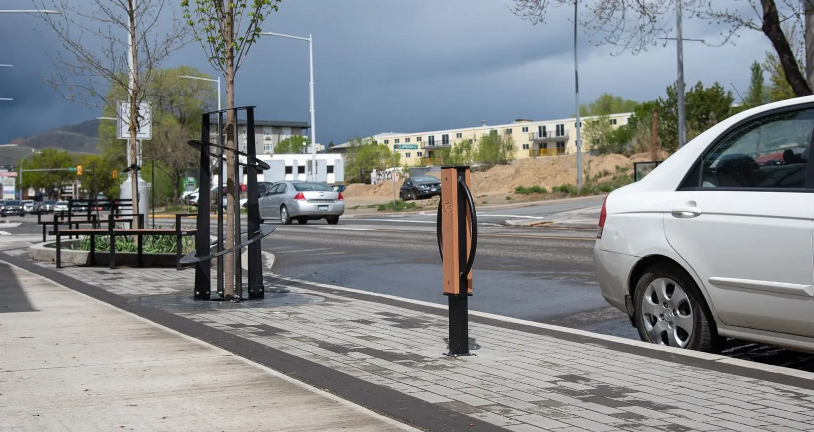 Streetscape featuring benches, tree guards, and a bike repair station. The site furniture enhances the pedestrian zone along the city street.