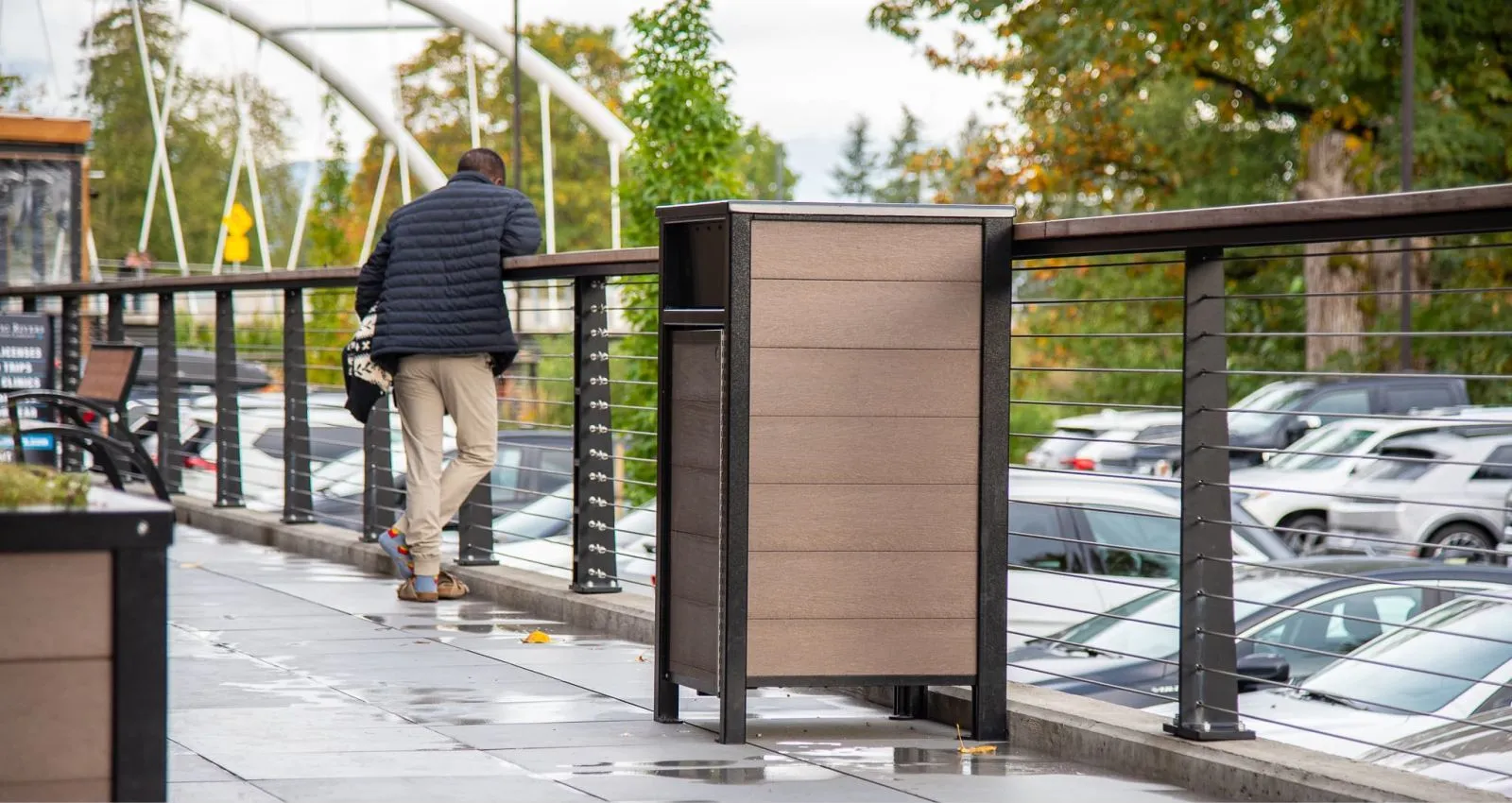 Urban Form large capacity commercial waste receptacle with recycled plastic lumber and powder-coated metal frame. This bin is located on a paved walkway with a bridge in the background.