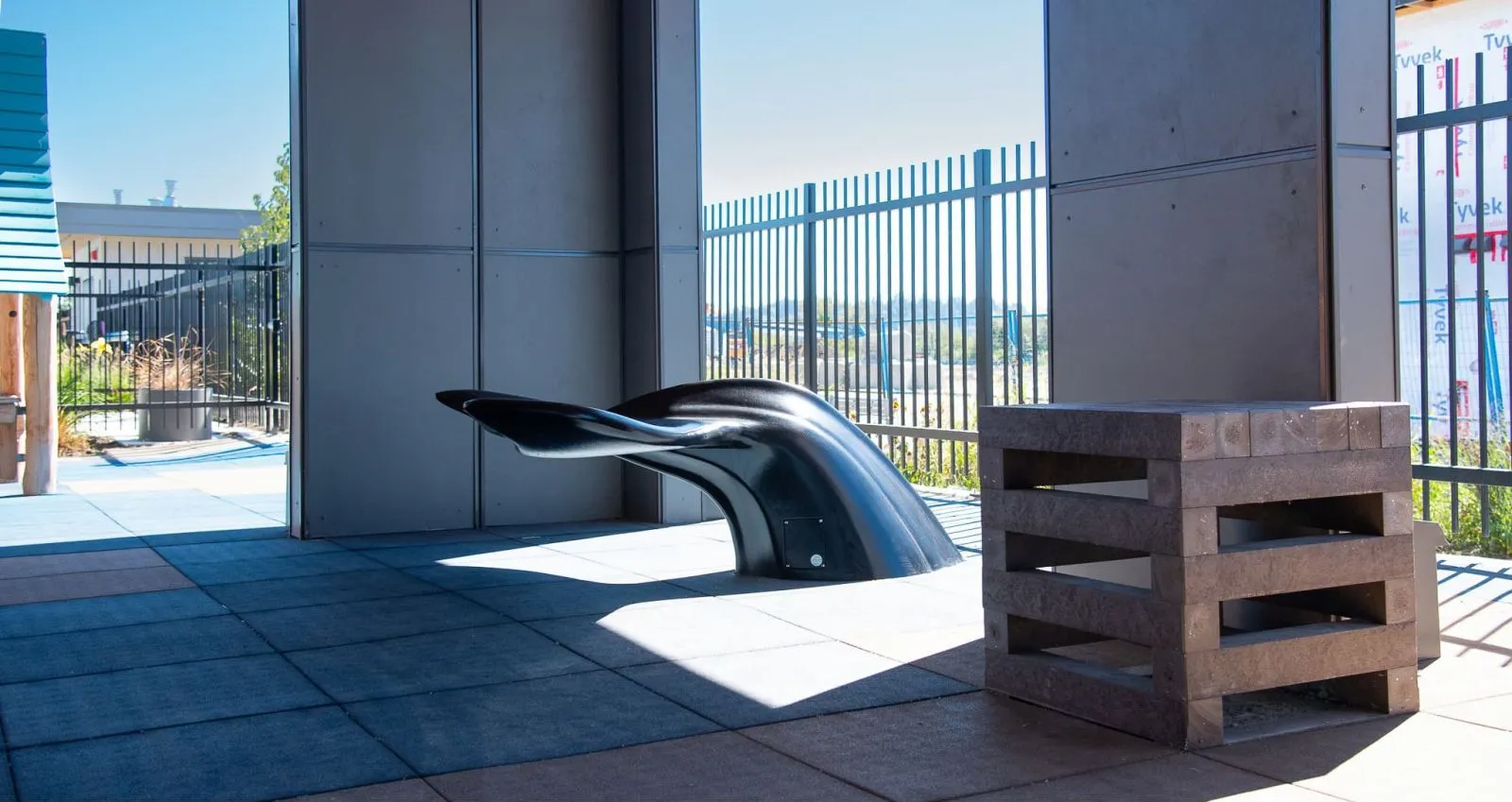 A Whale Tail Bench in a covered outdoor area, paired with a Perma-Step made from recycled plastic lumber. This functional art piece adds a unique seating option to the Boardwalk Development.