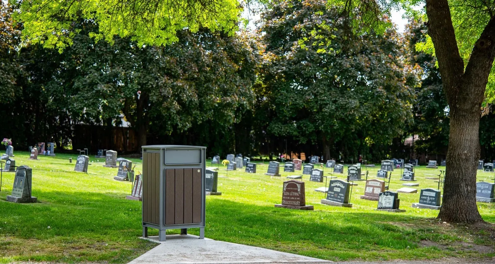 Beselt Square Top Waste Receptacle in a cemetery setting. The bin features recycled plastic lumber and a powder-coated metal frame.