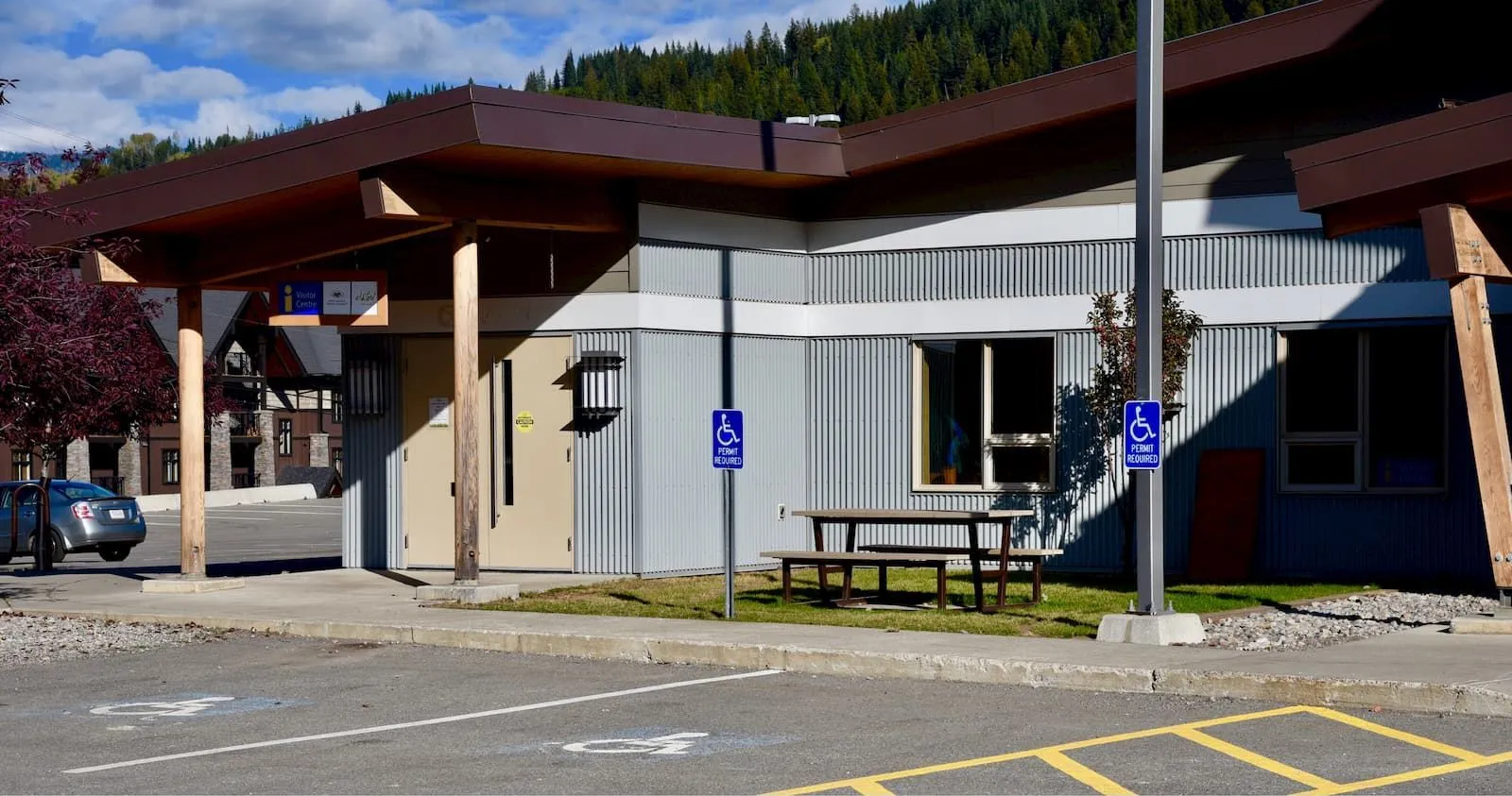 A Rutherford Picnic Table sits outside a building with accessible parking in Elkford, British Columbia. The table features a simple design with a wooden top and metal frame.