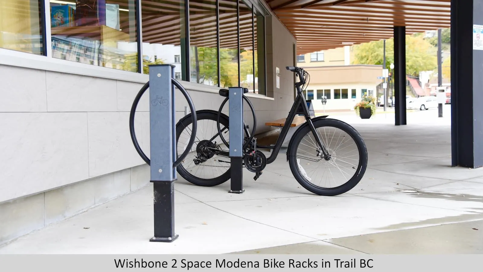 Two Modena 2 Space Bike Racks provide secure bicycle parking outside a building. The racks feature a powder-coated finish and are installed on a concrete surface.