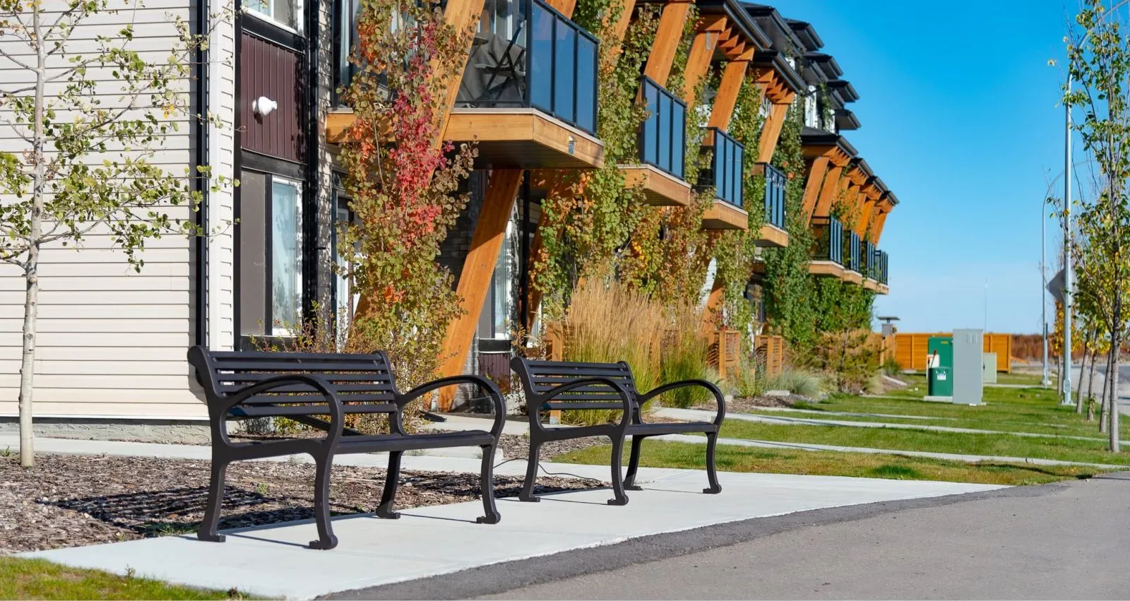Two Mountain Classic benches provide seating in a landscaped area. The benches feature a black finish and are placed on a concrete walkway.