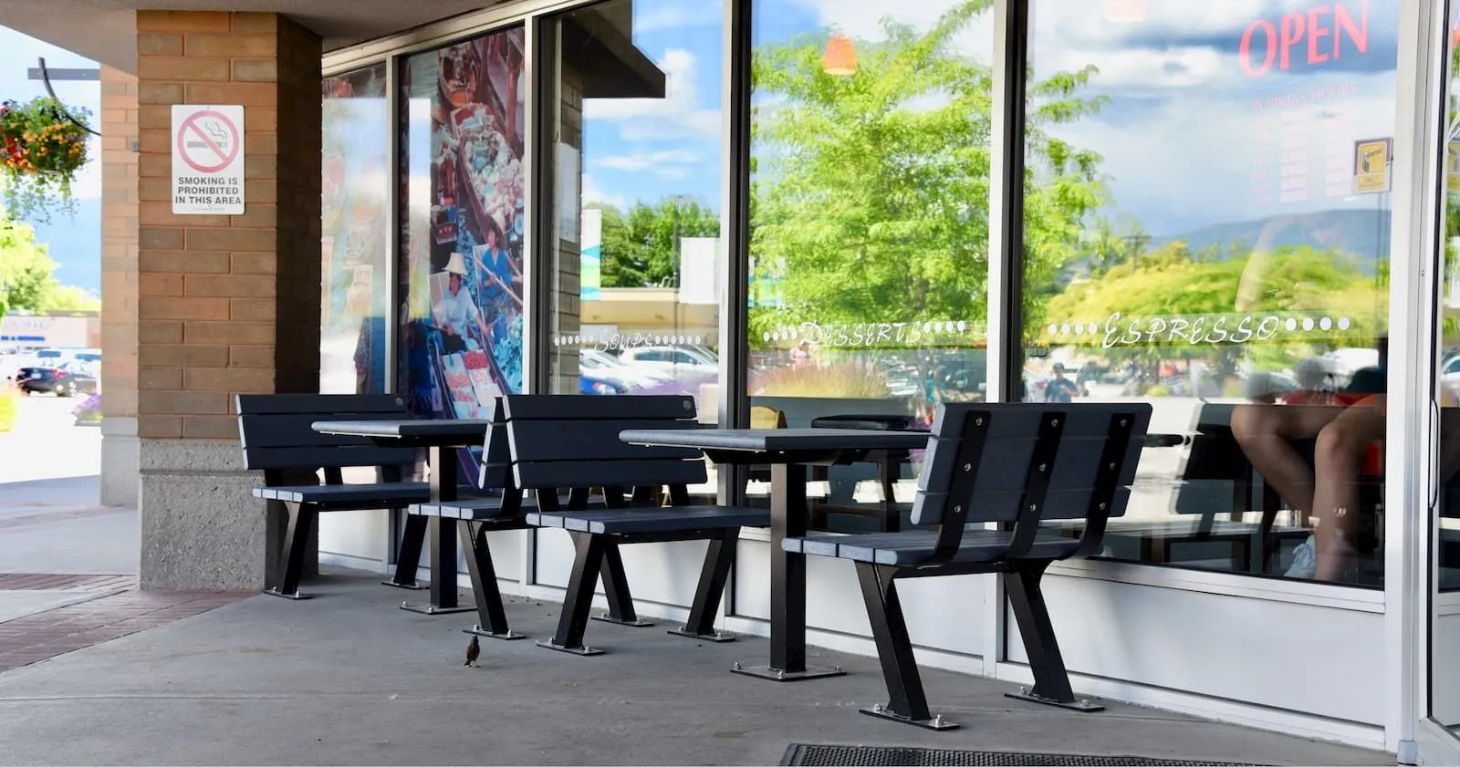 Bayview benches and tables provide outdoor seating outside a cafe. The furniture features recycled plastic lumber and powder-coated metal frames.