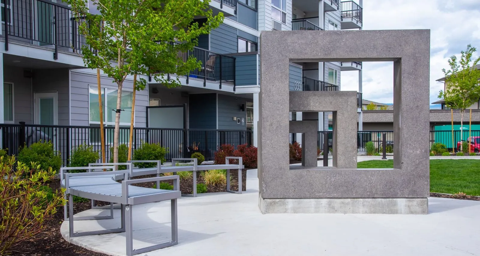 Skyline curved benches provide seating in an outdoor space near modern apartments. The benches feature a sleek design and complement the contemporary architecture.