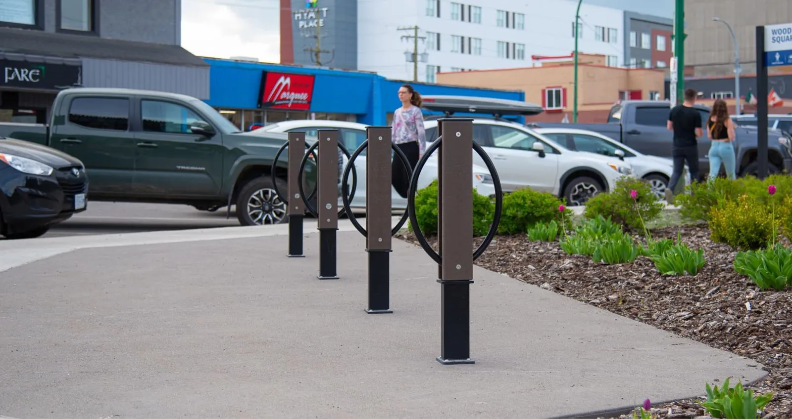 Modena 2 Space Bike Racks provide secure bicycle parking in a commercial area. The racks feature recycled plastic lumber uprights and powder-coated metal hoops.