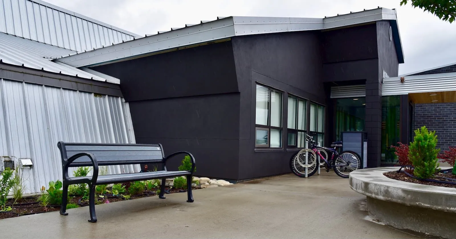 A Mountain Classic bench provides seating outside a modern building. The bench features black recycled plastic lumber and a black powder-coated frame.