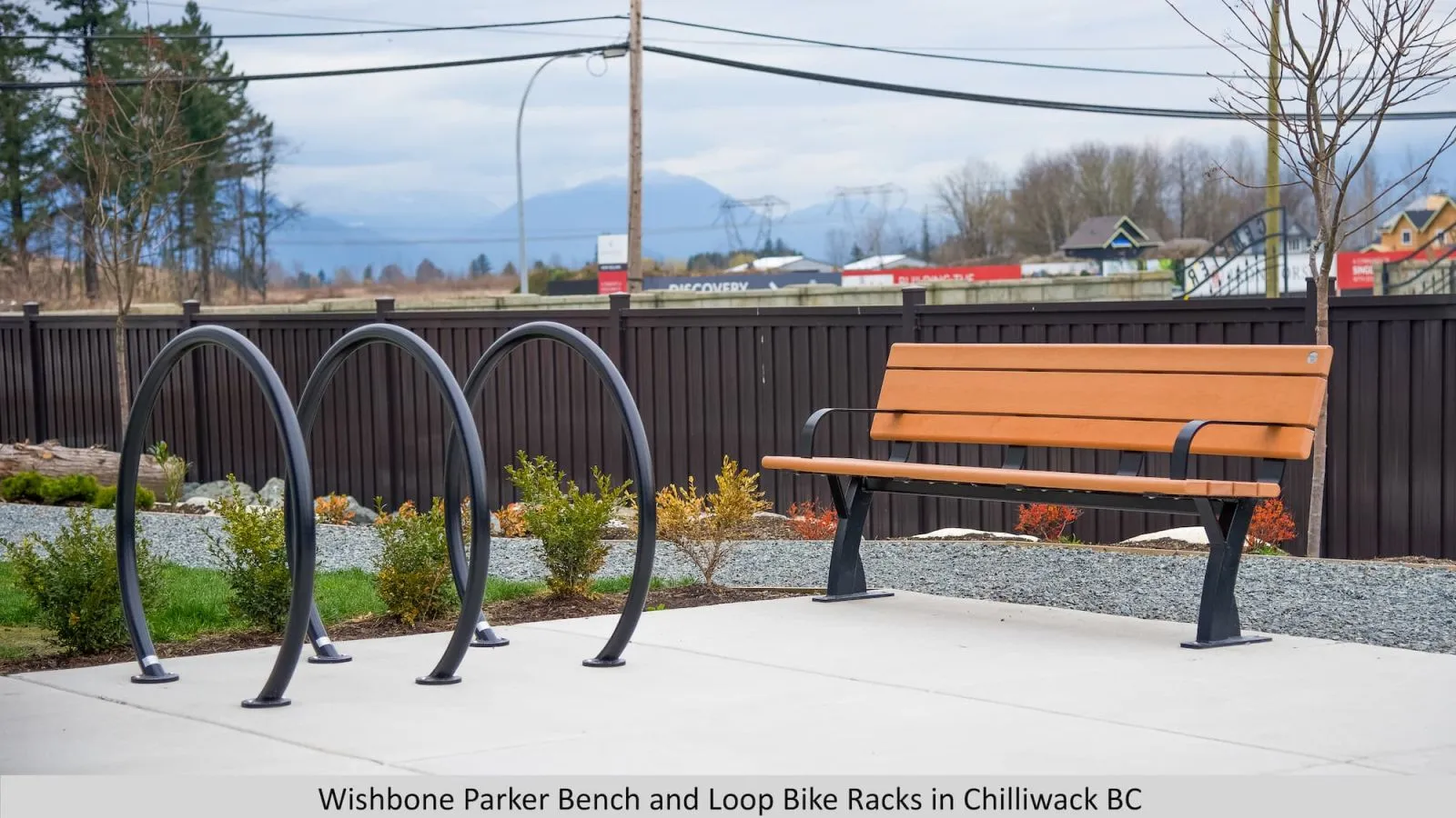 The Parker bench and Loop bike racks provide a comfortable seating and bike parking solution. The bench features recycled plastic lumber and a black powder-coated frame, complementing the sleek design of the bike racks.