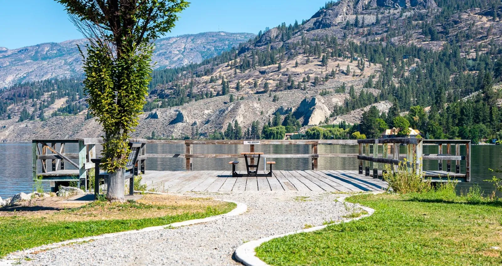 Heavy-duty picnic table on a wooden wharf overlooking a lake and mountains. The table features a black frame and wooden top and seats.