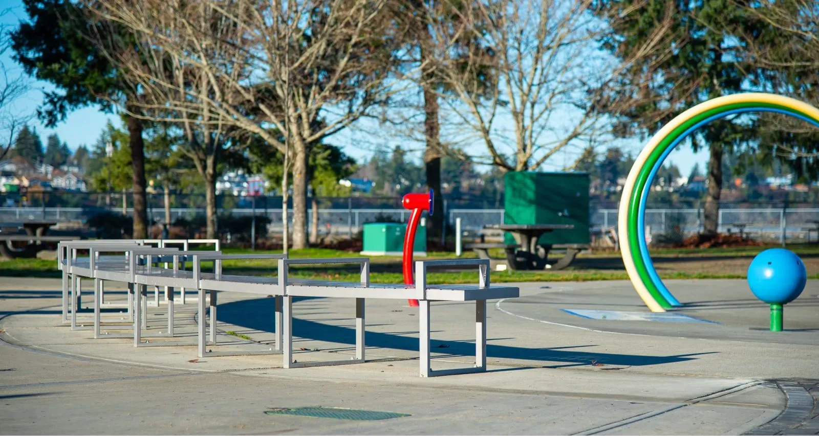 Skyline Curved Bench provides seating at a park. The bench features a metal frame and recycled plastic lumber.