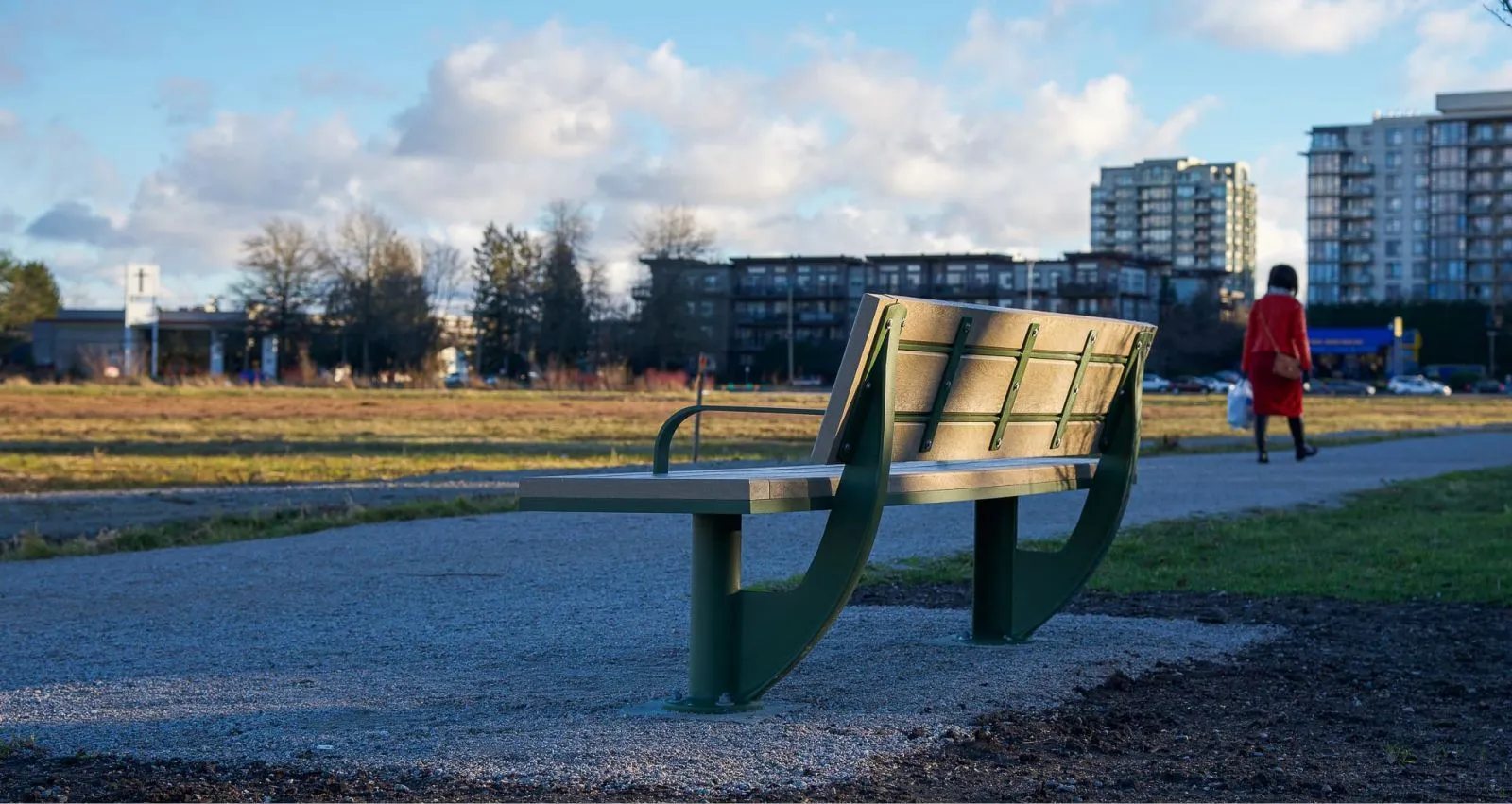 SurRe bench provides comfortable seating along a gravel path. The bench features recycled plastic lumber and a durable powder-coated frame, ideal for outdoor public spaces.