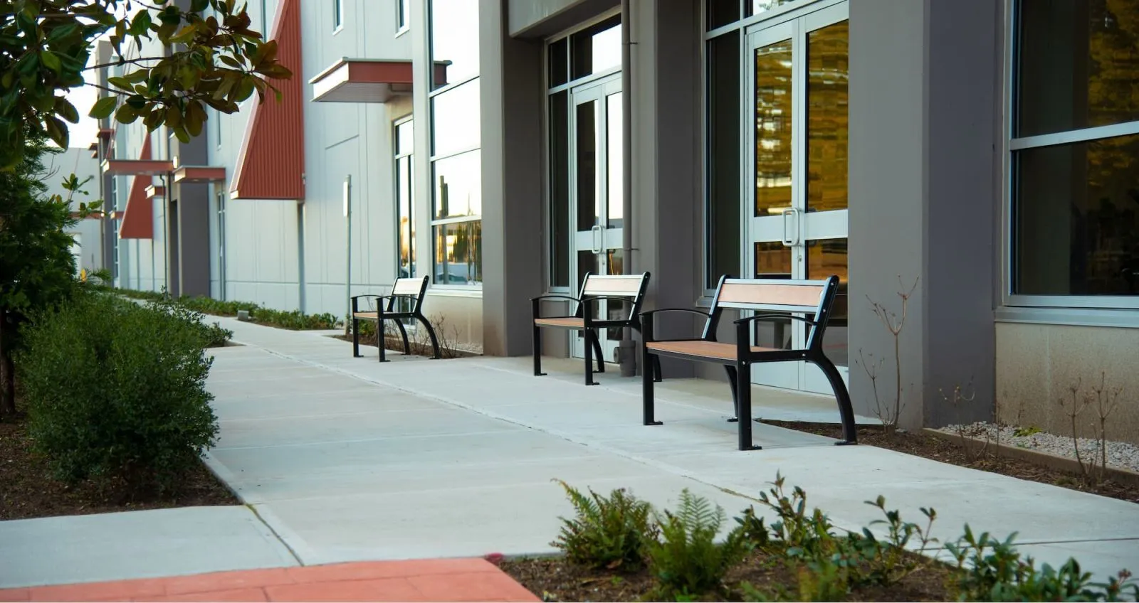 Durable benches provide seating along a walkway outside a modern building. The benches feature recycled plastic lumber and a black powder-coated frame.