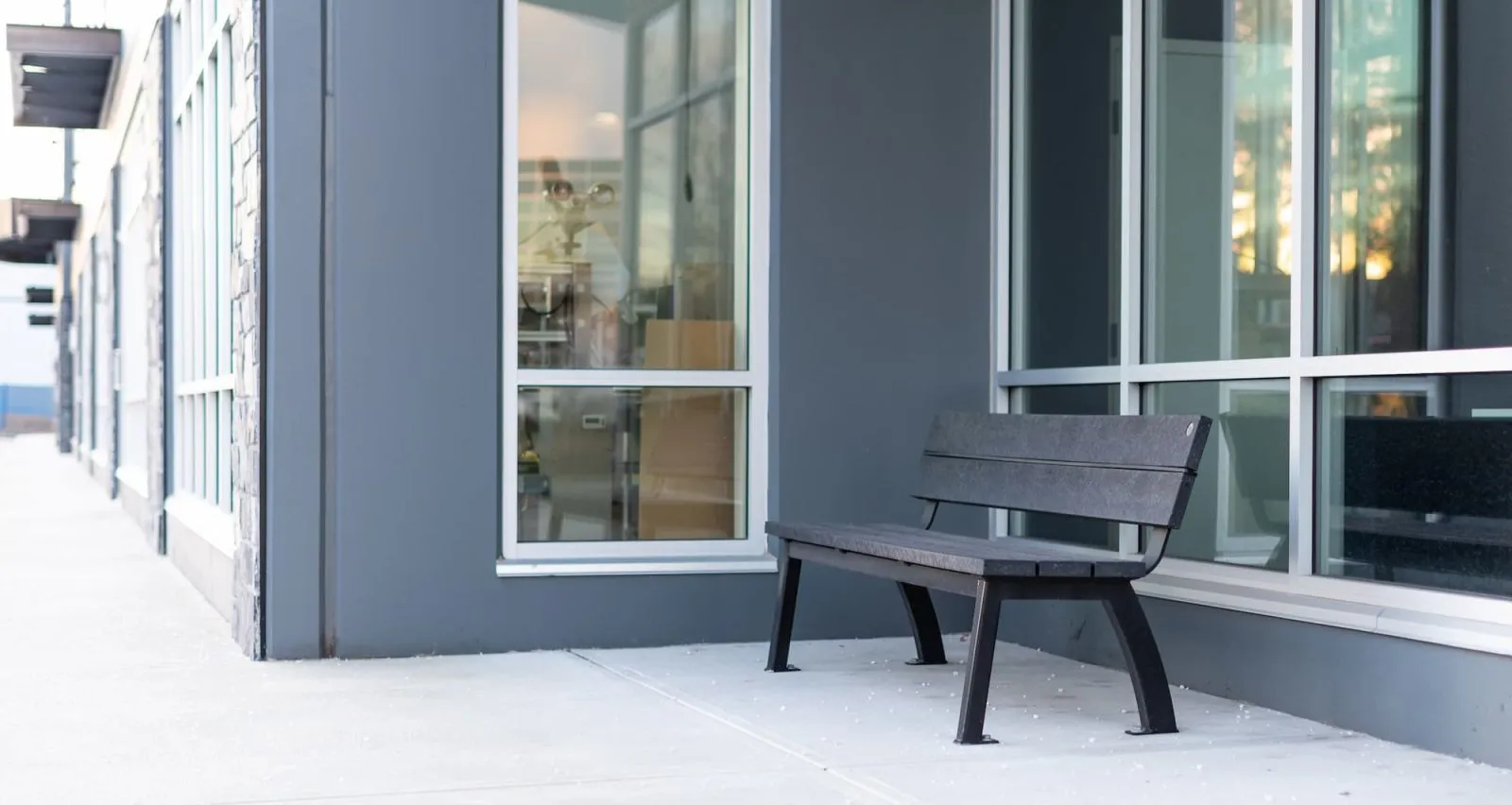 Aylesbury bench with recycled plastic lumber seating and black powder-coated frame, situated outside a modern building with large windows. This bench offers a comfortable and stylish seating solution for commercial or public spaces.