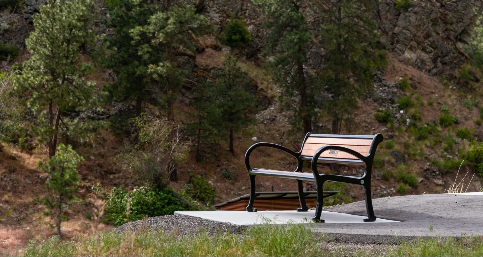 A Mountain Classic Wide Body Memorial Bench provides a place to rest in Heritage Hills Park. The bench is set on a concrete pad overlooking a natural hillside landscape near Okanagan Falls, British Columbia.