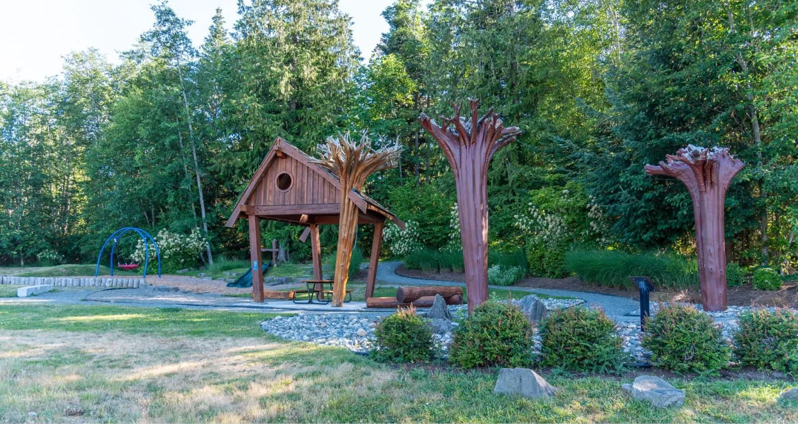 A Pipeline Picnic Table sits under a wooden shelter in Bowser, British Columbia. The area is surrounded by lush greenery and trees.