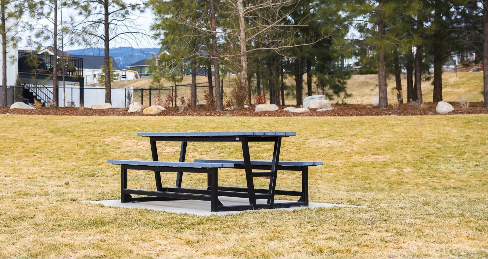 Heavy-duty picnic table with black frame and grey recycled plastic lumber top and seats. This durable table provides a comfortable outdoor dining space in a park setting.