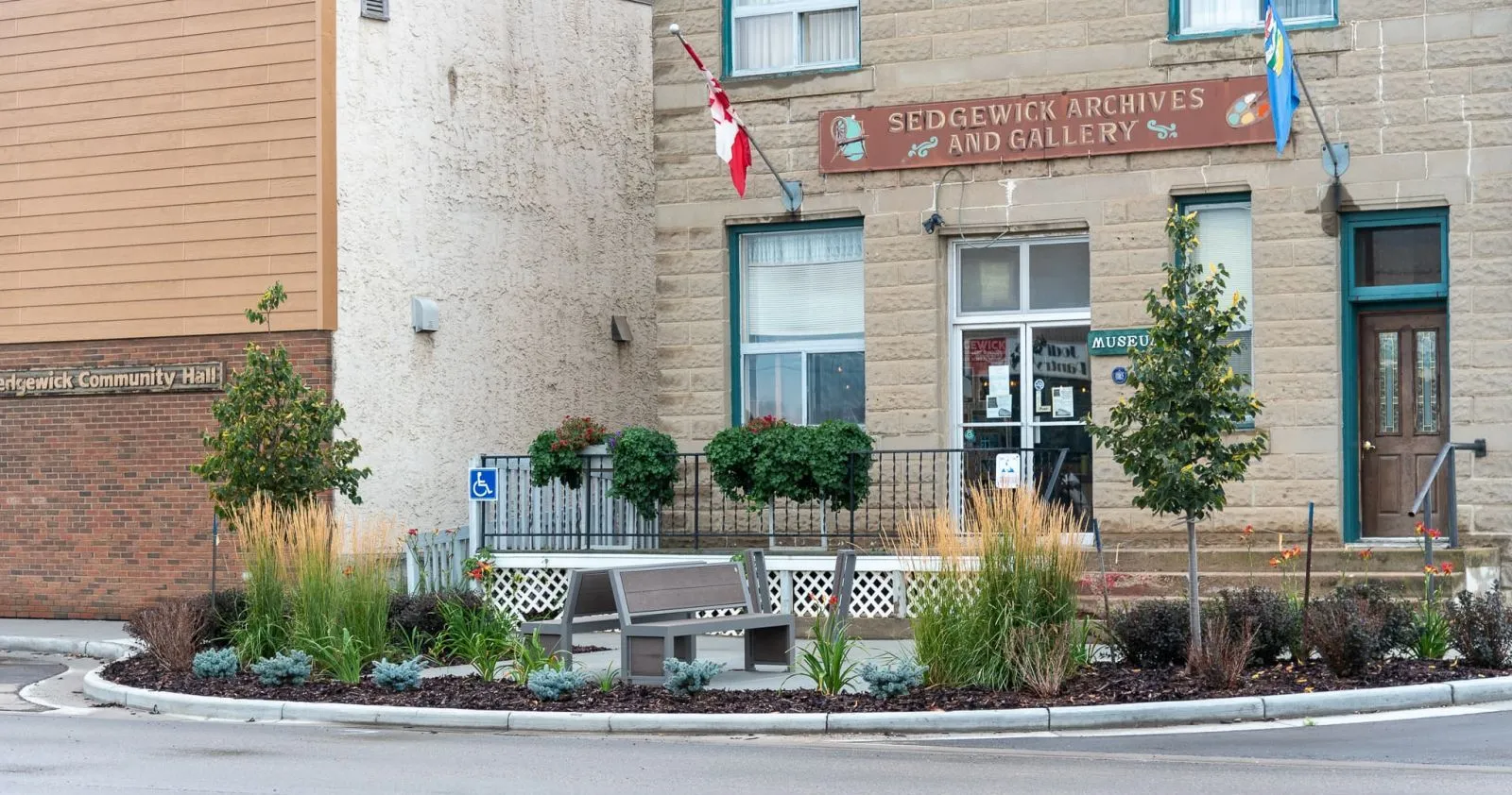 Urban Form Full Back bench provides seating in front of the Sedgewick Archives and Gallery and Sedgewick Community Hall. The bench is surrounded by landscaping and adds to the curb appeal of the building.