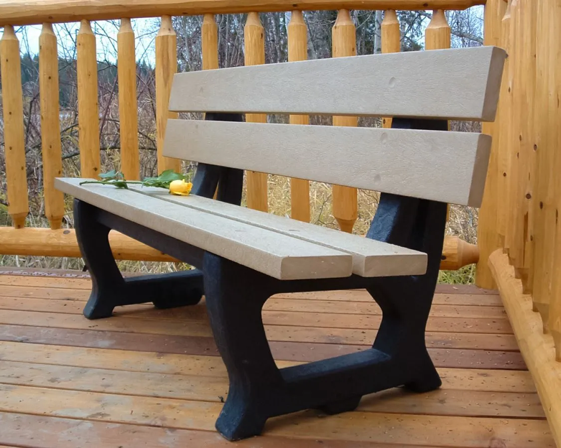 A Deco bench with recycled plastic lumber seating and a black frame sits on a wooden deck. The bench is adorned with a yellow rose.
