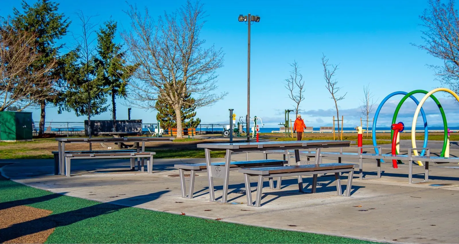 Wheelchair accessible picnic tables provide an inclusive outdoor dining space. The tables feature durable recycled plastic lumber and powder-coated metal frames, set in a waterfront park with recreational facilities.