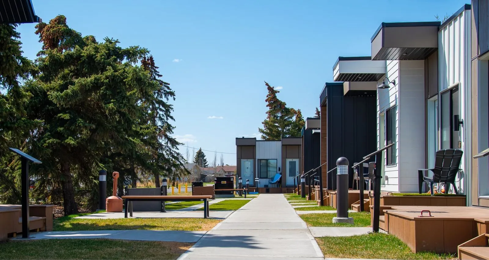 Aylesbury Backless Benches provide seating along a walkway at the Atco Veterans Village in Edmonton, Alberta. The benches feature a simple design with recycled plastic lumber.