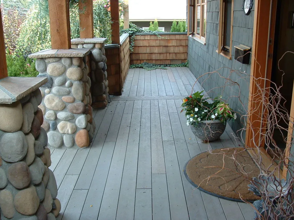 A residential porch features decking made from recycled plastic lumber. The porch is supported by stone pillars and has a shingled wall.