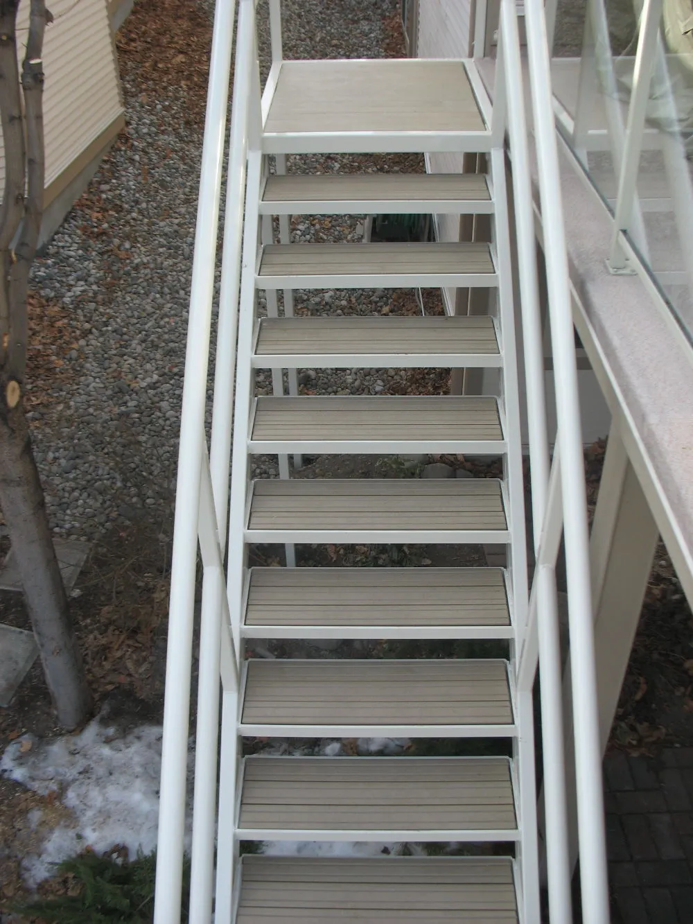 Staircase with white metal frame and Sand-colored recycled plastic lumber steps. The steps lead up to a landing with a glass railing.