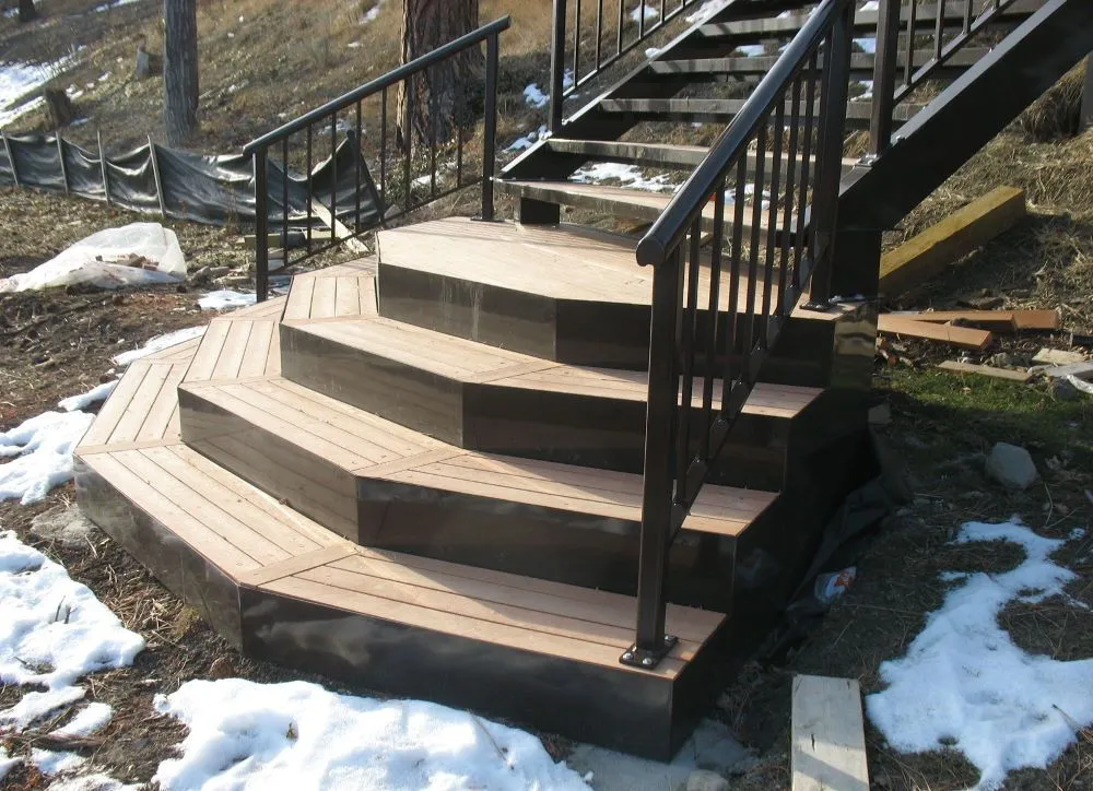 Staircase with recycled plastic lumber steps and black metal railings. The steps are a light wood color with dark brown trim.