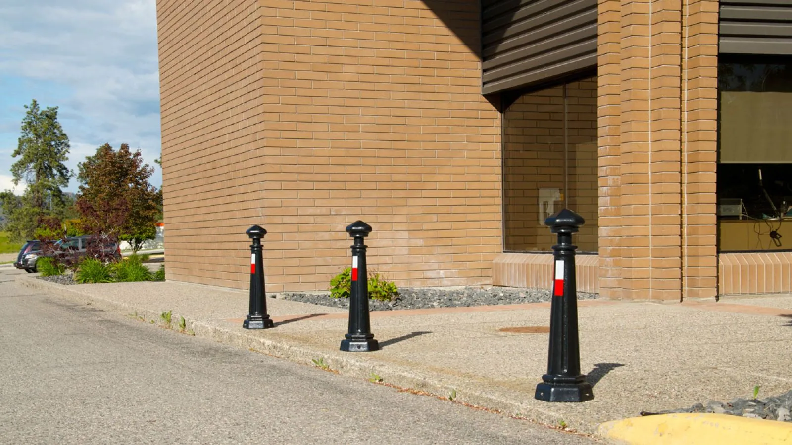 Classic bollards provide pedestrian safety and traffic control near a brick building. These bollards feature a black powder coat finish and reflective safety bands.
