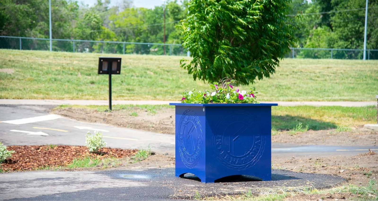 A Beselt Square Planter adds a touch of color to a park or public space. This planter features a custom logo and is finished in a vibrant blue powder coat.