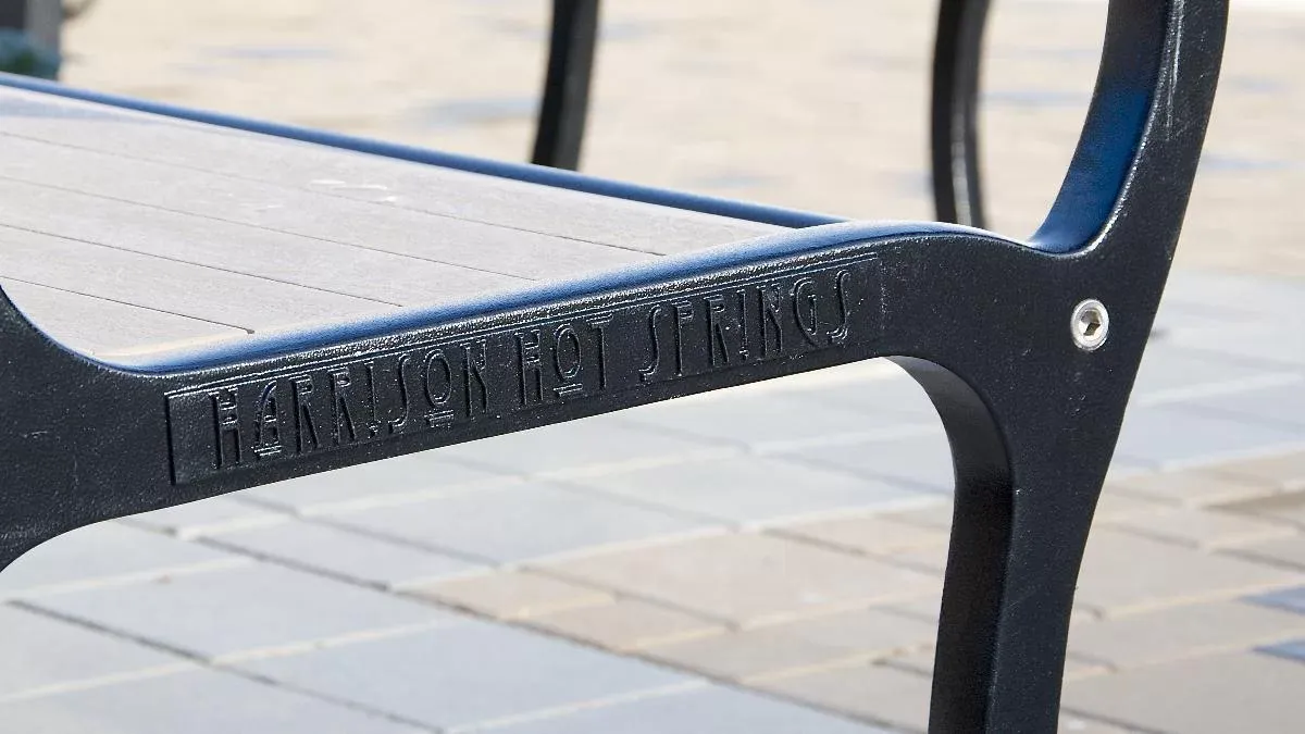 Close-up of a bench with custom casting displaying "Harrison Hot Springs". The bench features black recycled plastic lumber and a black powder-coated frame.