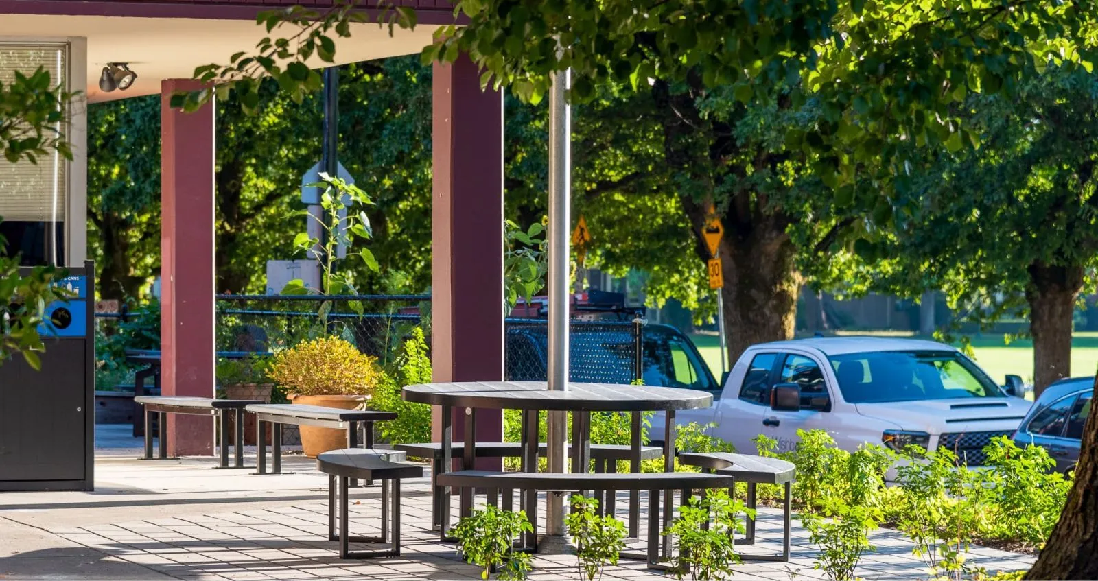 Skyline 5 ft Round Flagpole Picnic Table provides a central gathering spot at Fraser Academy in Vancouver, BC. The table features a circular design with attached seating, perfect for outdoor dining and socializing.