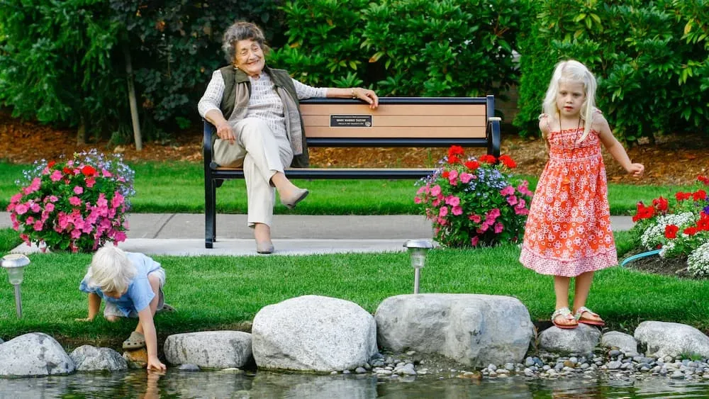Classic bench provides seating in a garden setting with a pond. The bench features recycled plastic lumber and a black powder-coated frame.