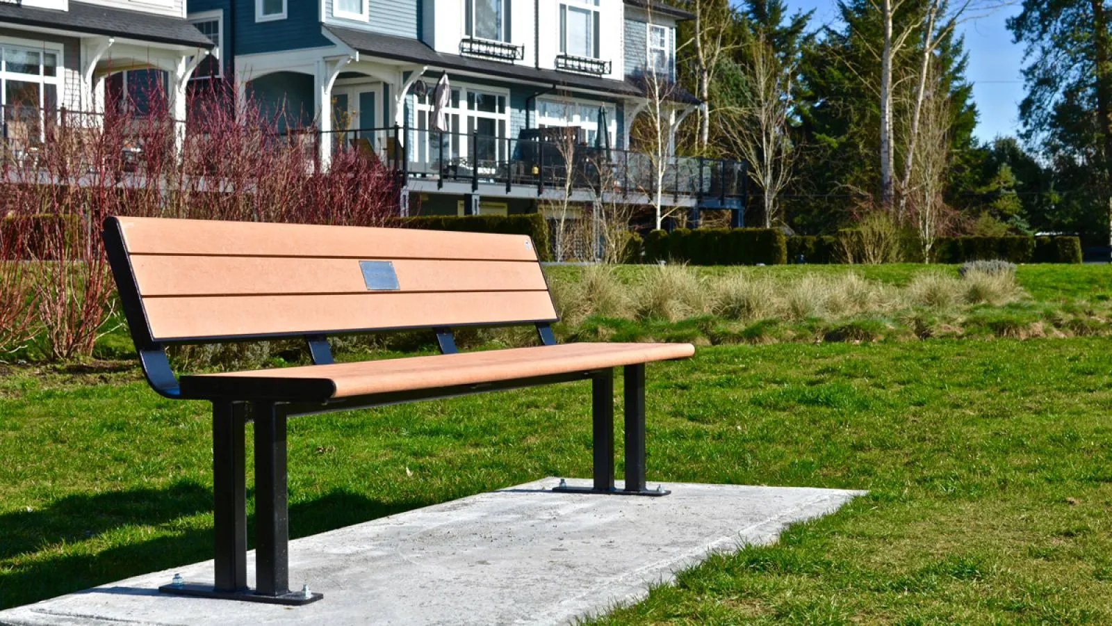 A Larson bench provides seating in a grassy area. The bench features recycled plastic lumber and a black powder-coated frame.