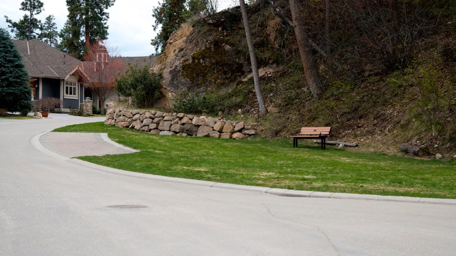 A Larson bench with direct burial legs sits on a grassy area near a stone wall at Predator Ridge Golf Resort. This bench offers a comfortable and durable seating option for outdoor spaces.