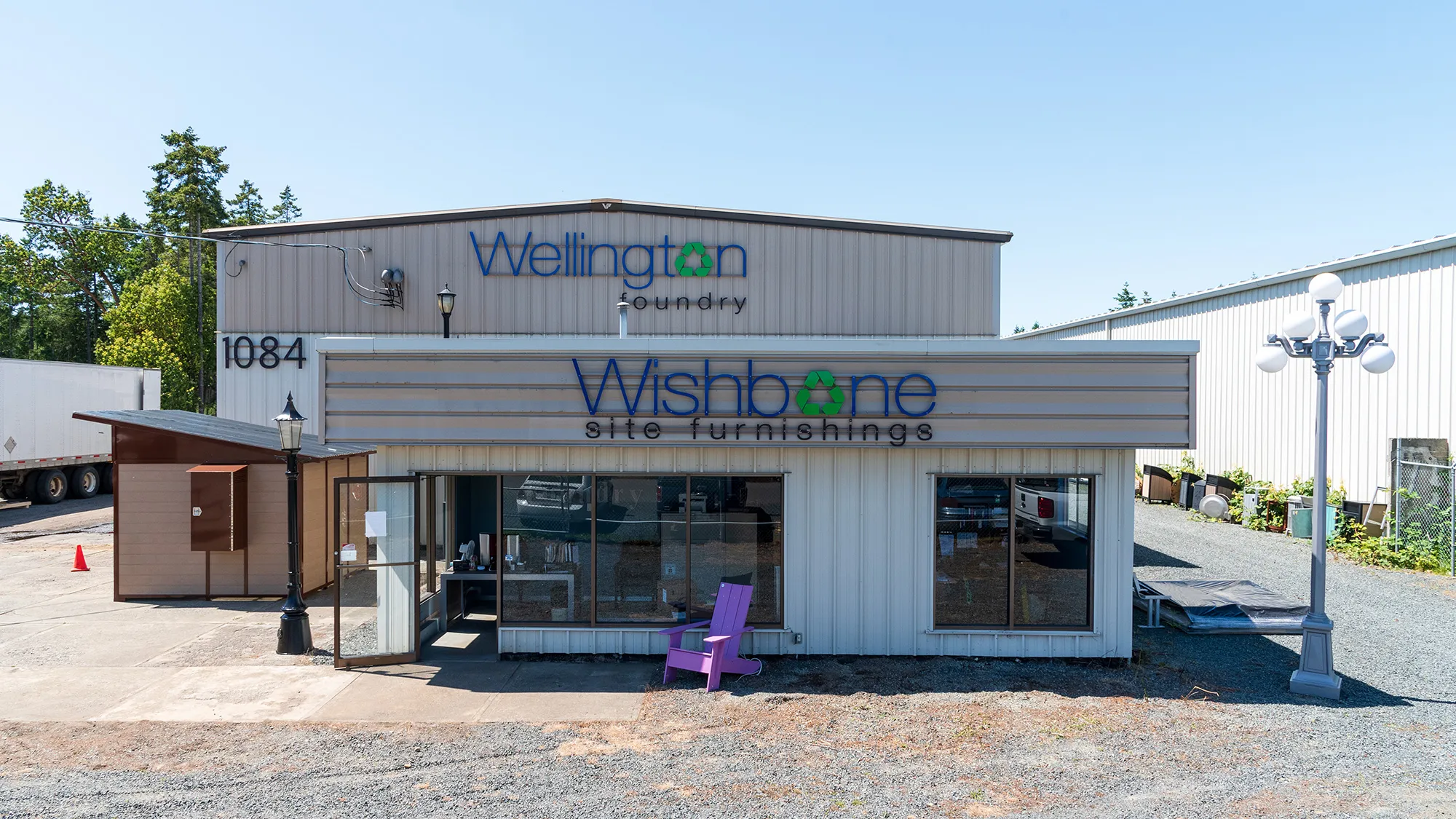 Exterior view of the manufacturing facility in Parksville, BC, showcasing the company signage. A purple Giant Adirondack Chair sits outside the entrance.