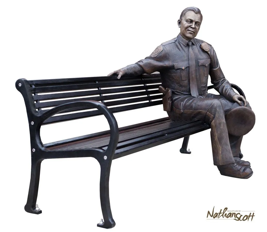 All-metal bench with a bronze statue of a police officer sitting on it. The bench features a black powder coat finish.