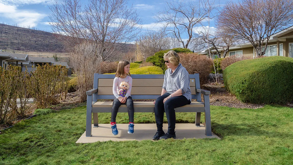 Rutherford bench provides comfortable seating in a landscaped area. The bench features recycled plastic lumber slats and a powder-coated metal frame.