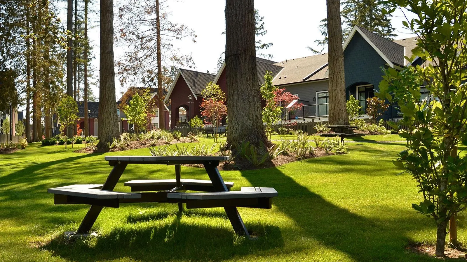 Hexagonal picnic table with recycled plastic lumber top and powder-coated frame in a landscaped residential area. The table provides a comfortable and durable space for outdoor dining and gathering.