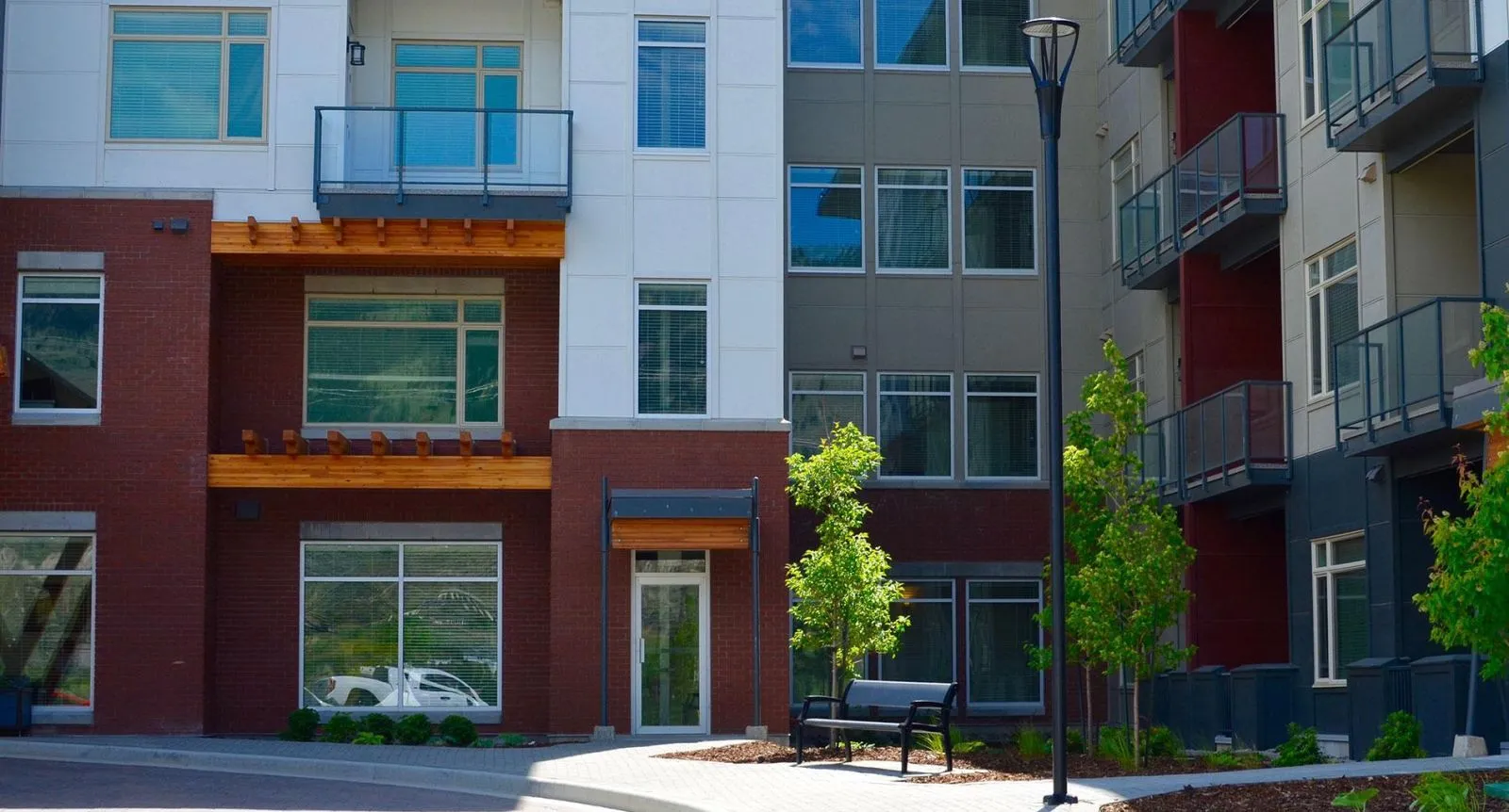 A black bench sits in front of a modern apartment building. The bench provides seating for residents and visitors to enjoy the outdoor space.