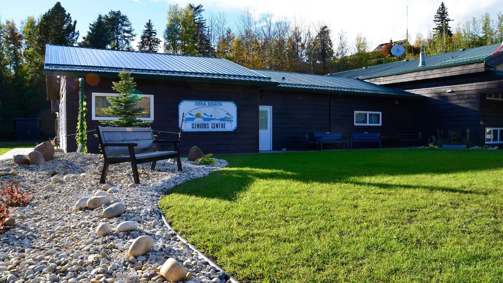 A Rutherford bench sits in front of the Seba Beach Seniors Centre in Alberta, Canada. The bench features recycled plastic lumber and a black powder-coated frame.