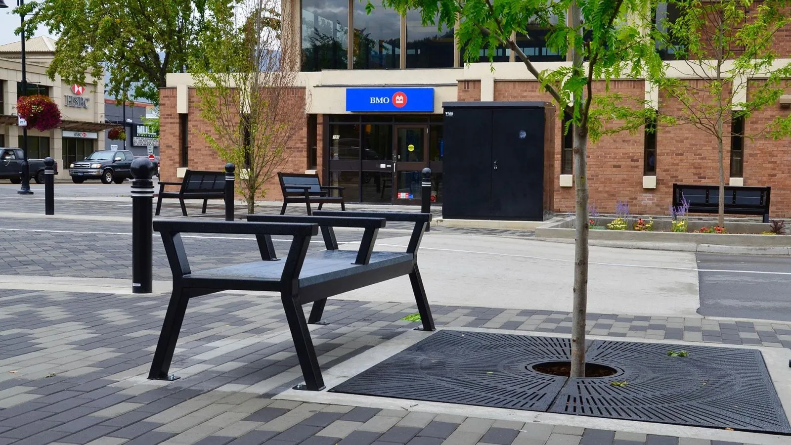 Rutherford benches provide seating in a pedestrian area. The benches feature a black powder coat finish.