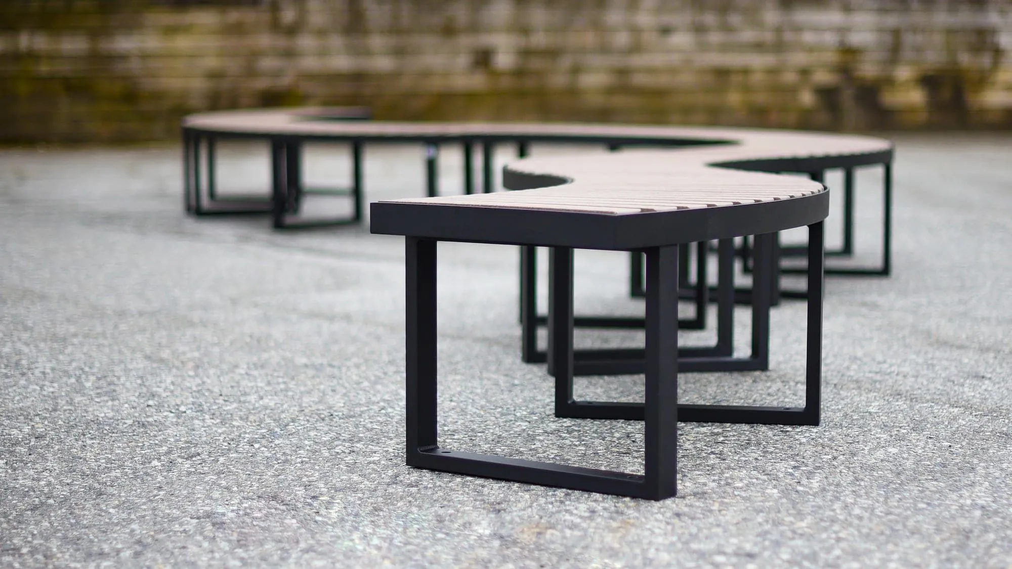 Curved park bench with recycled plastic lumber slats and a powder-coated metal frame provides comfortable seating in a public space. The modular design allows for flexible configurations.