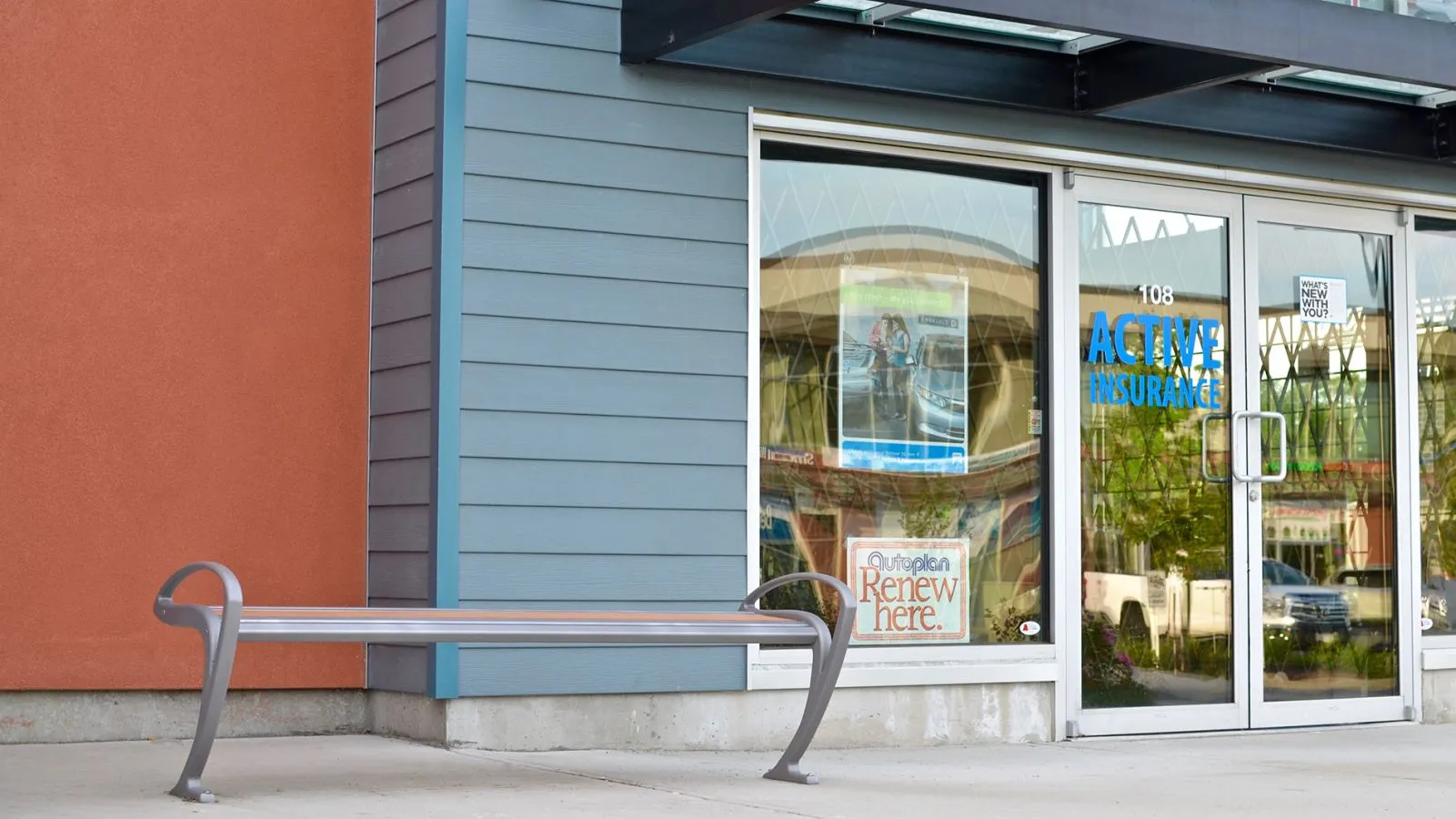 A TENAJ bench provides seating outside an insurance office. The bench features a silver-colored metal frame and light-colored recycled plastic lumber.