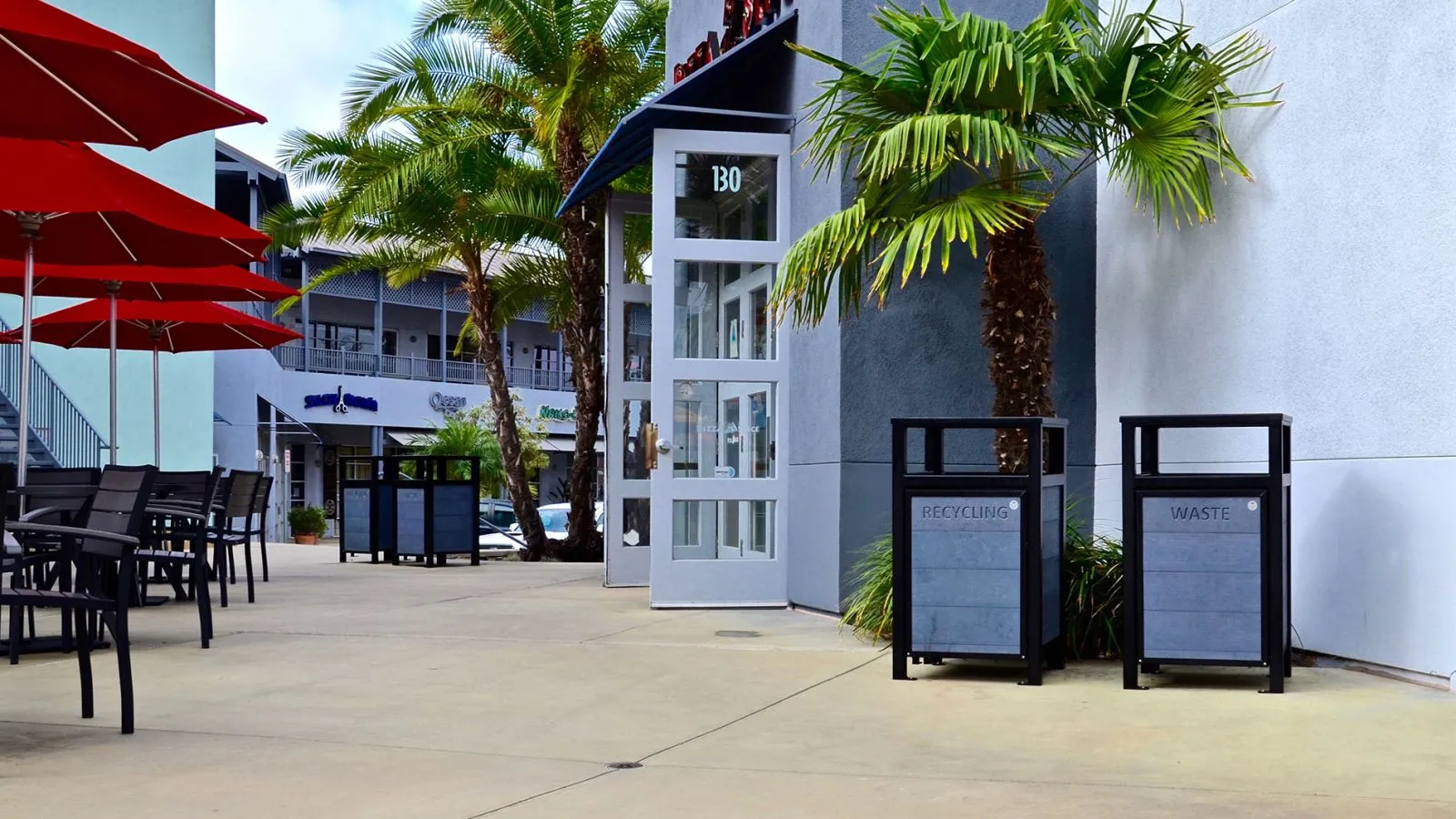 Urban Form waste and recycling receptacles provide convenient disposal options in a commercial setting. The receptacles feature a black frame and grey recycled plastic lumber.