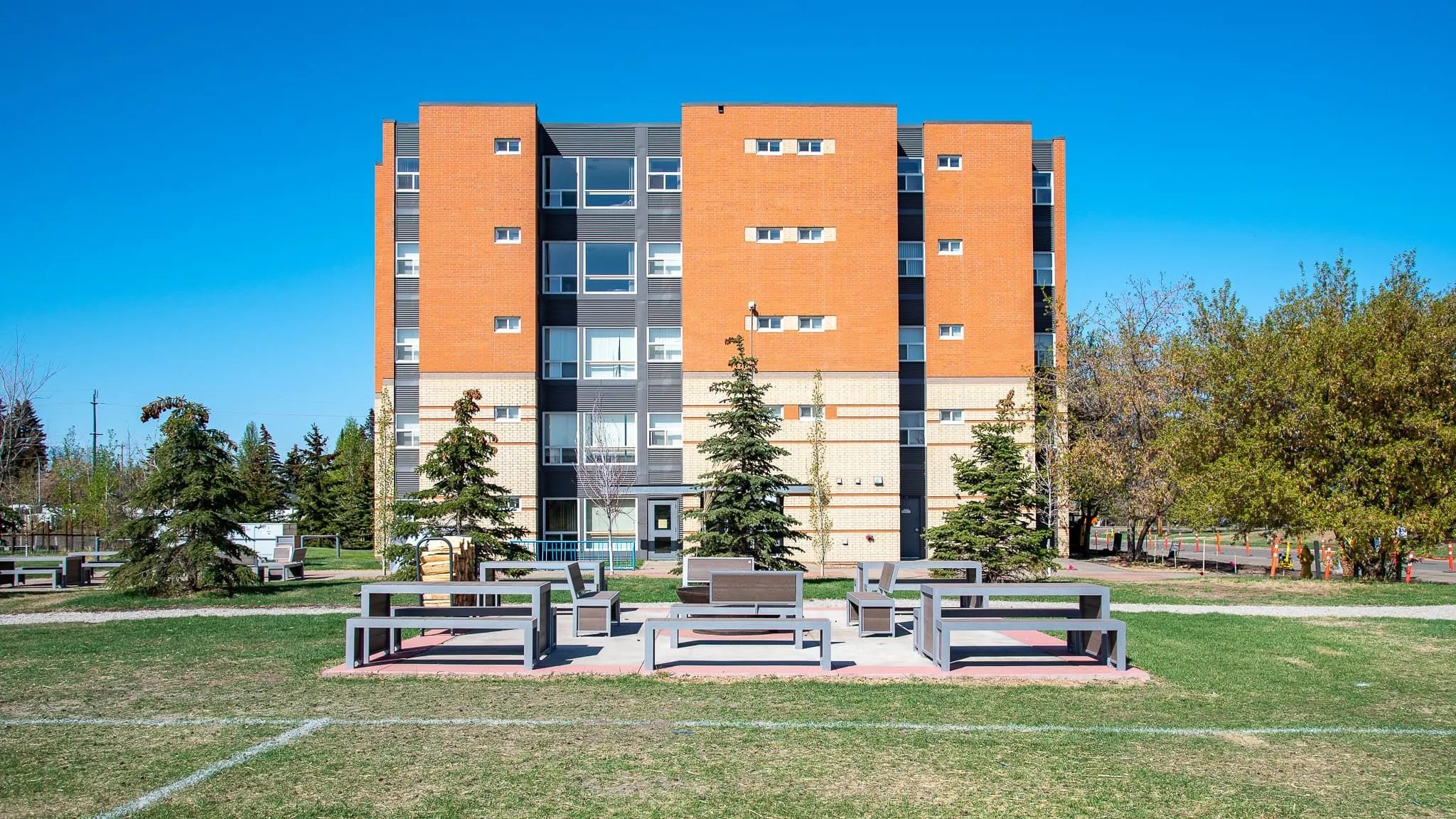 Outdoor seating area with Urban Form picnic tables and benches in front of a brick building. The site furniture provides a place for students to gather and relax on the Kings University campus.