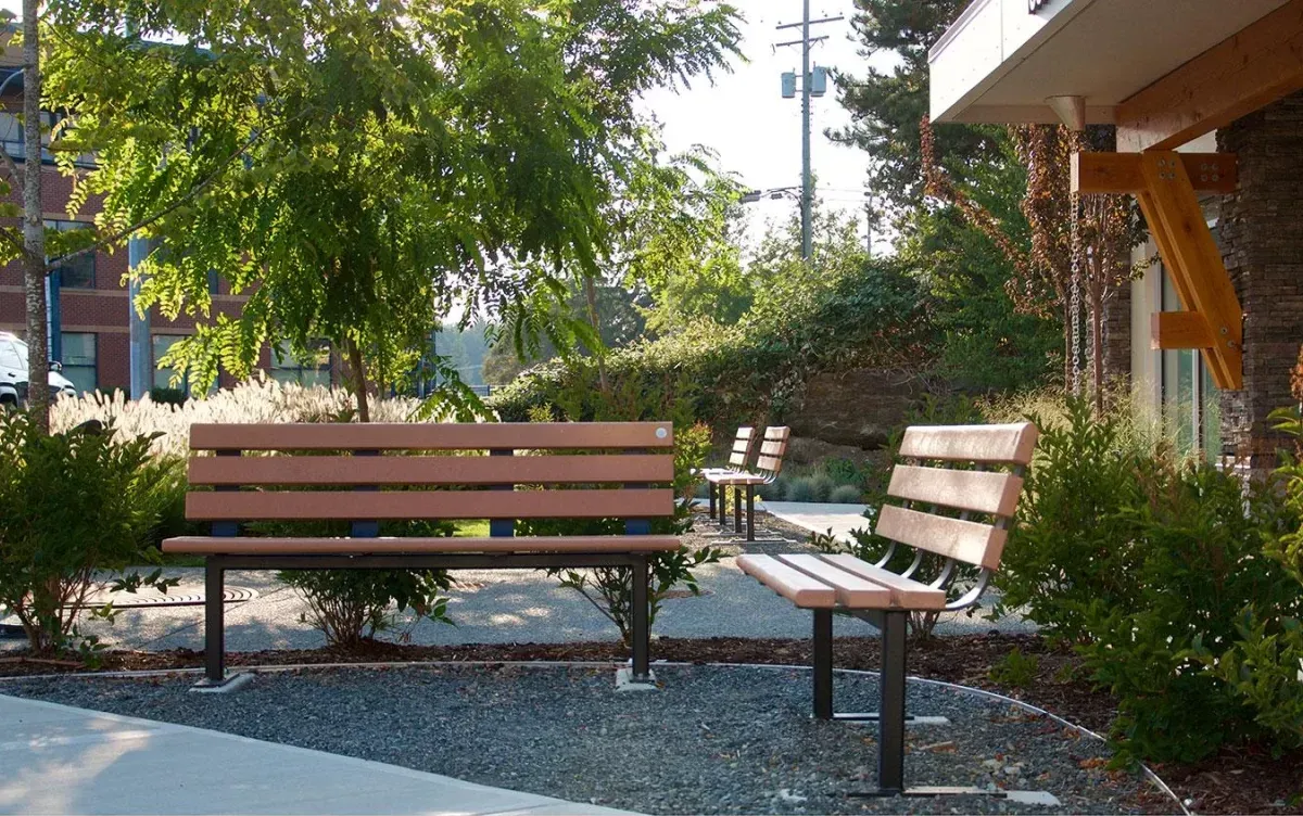 Durable benches provide comfortable seating in a landscaped outdoor area. The recycled plastic lumber and powder-coated metal construction ensures longevity and style.