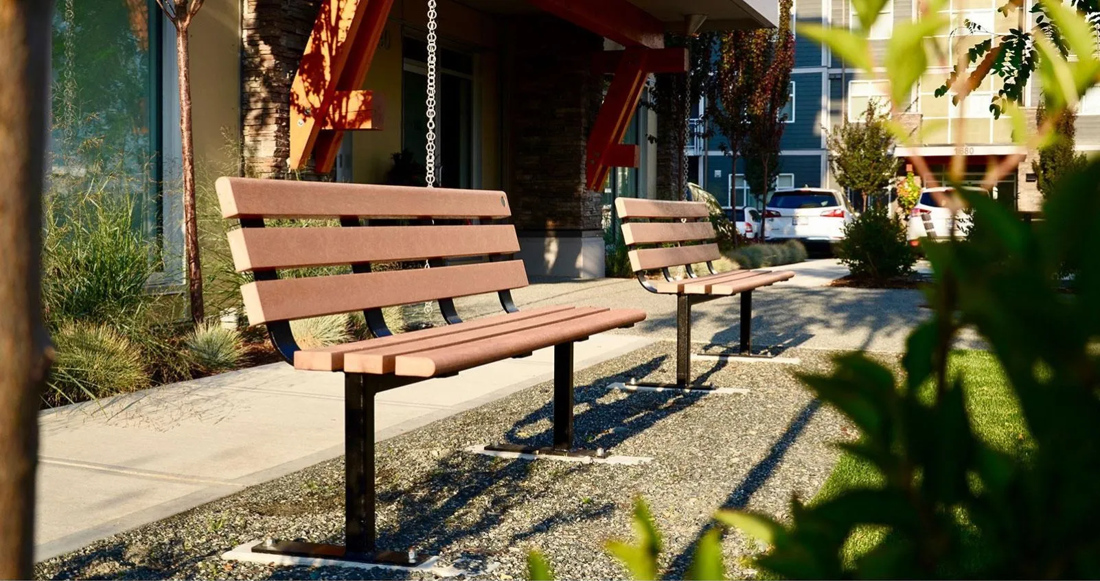 Two standard benches line a walkway outside an apartment building. The benches feature recycled plastic lumber and powder-coated metal frames.
