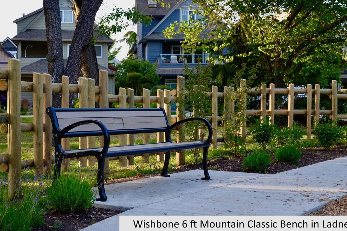 A Mountain Classic bench provides seating along a paved path in Ladner, British Columbia. The bench features recycled plastic lumber and a black powder-coated frame, complementing the surrounding residential area.